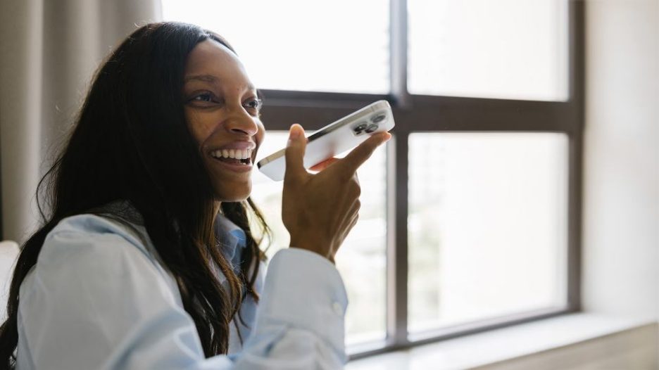 happy woman is sitting recording an audio message on a mobile phone